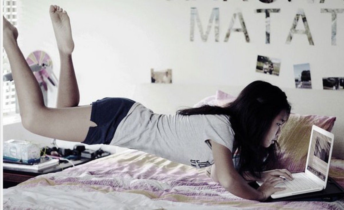 Asian girl levitating over her bed while using laptop