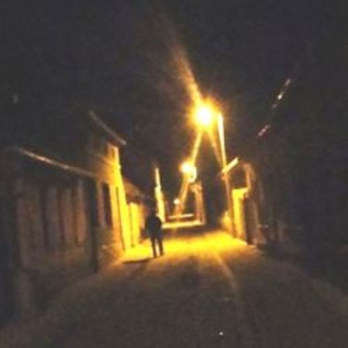 A tilted view of a person walking down a poorly-lit street at night.