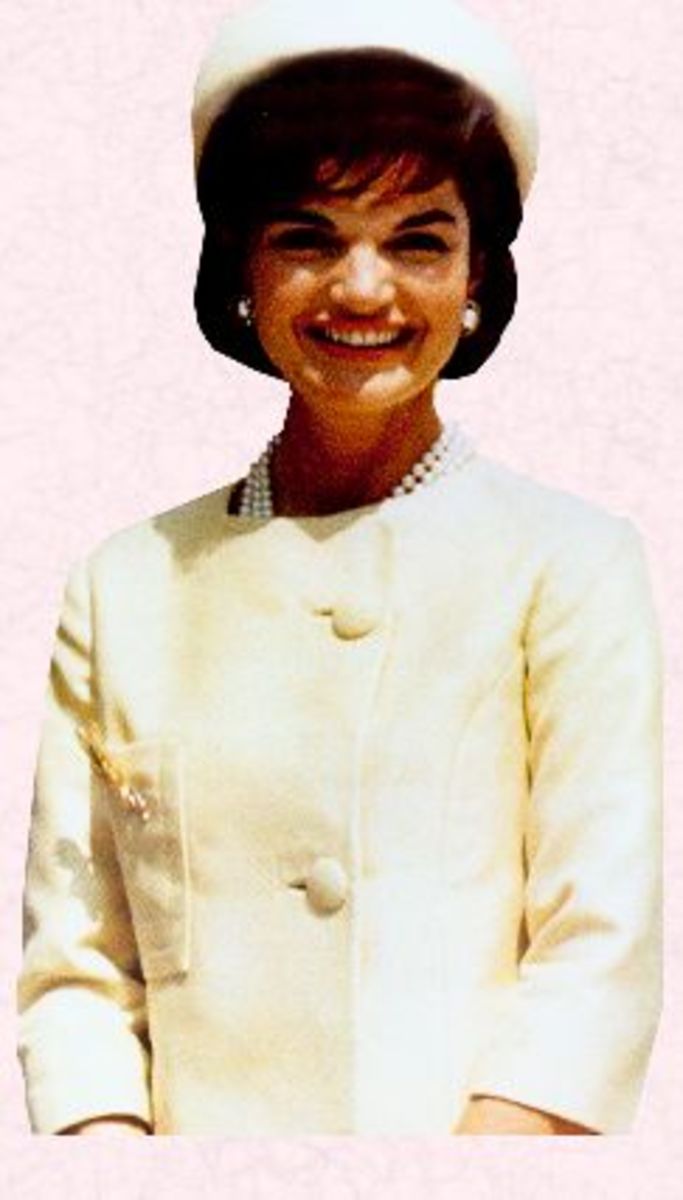 Jackie Kennedy wearing a light colored suit with matching hat and her three strand pearl necklace