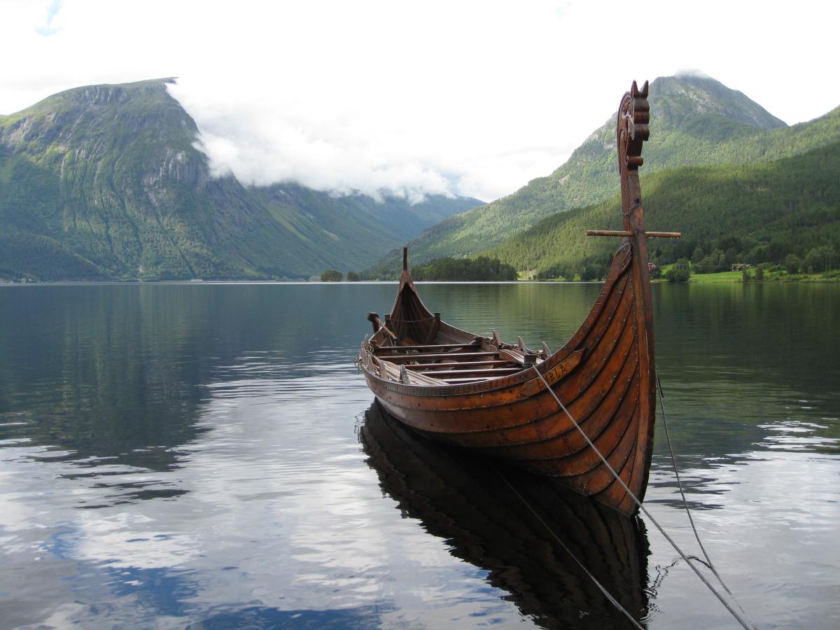 A sleek, narrow 'karve' rides at anchor in a fjord, awaiting a nobleman, or even a king 
