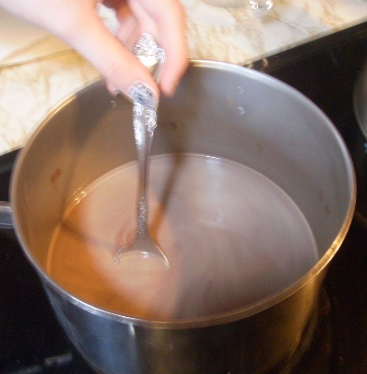 The blurry hand stirring the light-looking thin chocolate that will darken and thicken...
