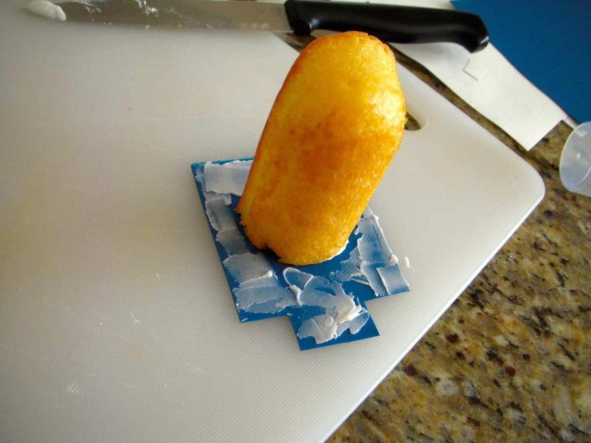 Step 4: Put overalls on the Twinkie. Carefully spread a small amount of icing on the Sugar Sheet overalls and place the Twinkie, cut side down, in the center.Note the overall "bib" is in front.