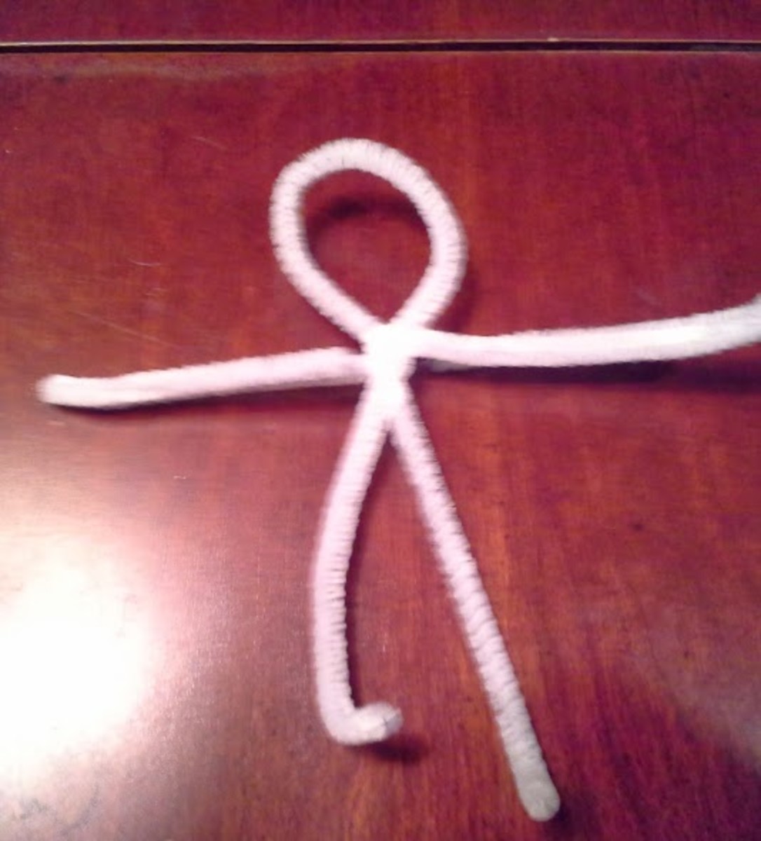 Twist the other pipe cleaner at the very bottom of the loop to make the arms.  They need to be cropped using a wire cutter to the desired length.  Do not forget to curl up the ends to avoid sharp edges.