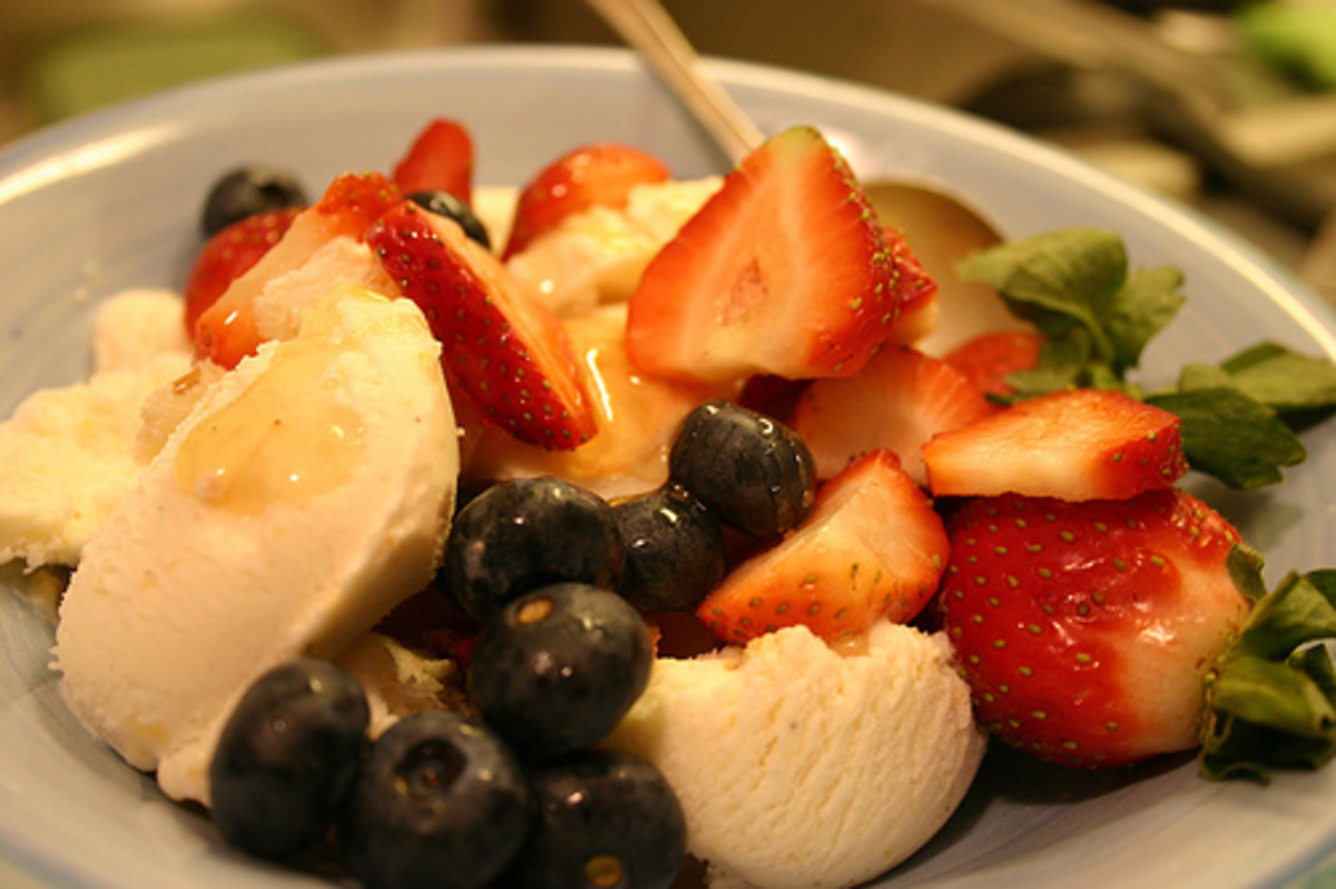 Peach ice cream with strawberries and blueberries topped with honey.