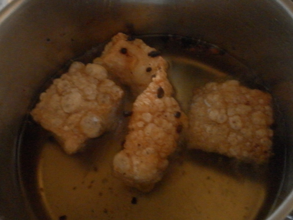 Pork rind turning into pork cracklings in a pot of hot oil.