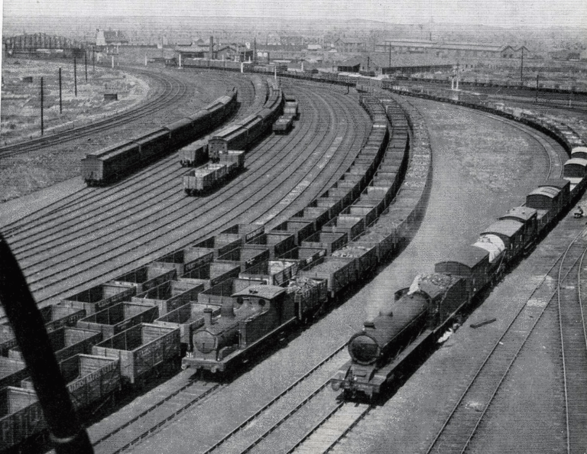 1941, private owner coal wagons lined up in sidings for war traffic. Due to the shortage of open wagon stock they would not only be used on coal trains. A very long mixed freight train rounds the curve on the right 