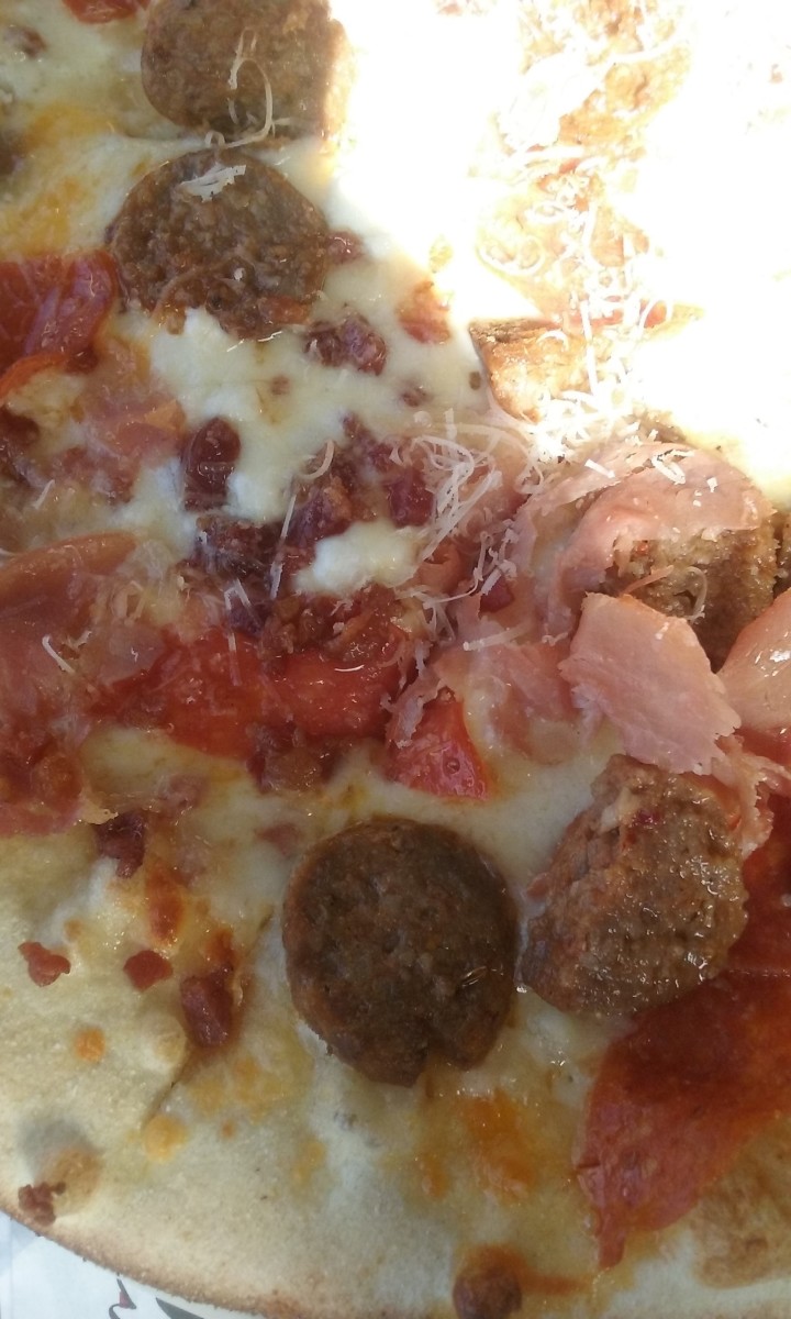 A flat bread pizza served with various meat toppings including sausage and ham