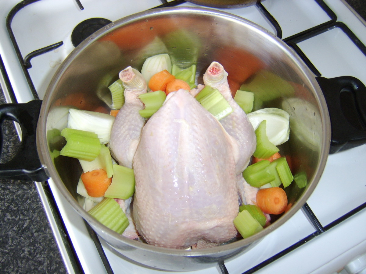 The whole chicken is laid on top of the vegetables in a large pot