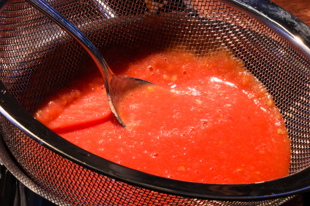 Pouring pureed tomatoes through a sieve.