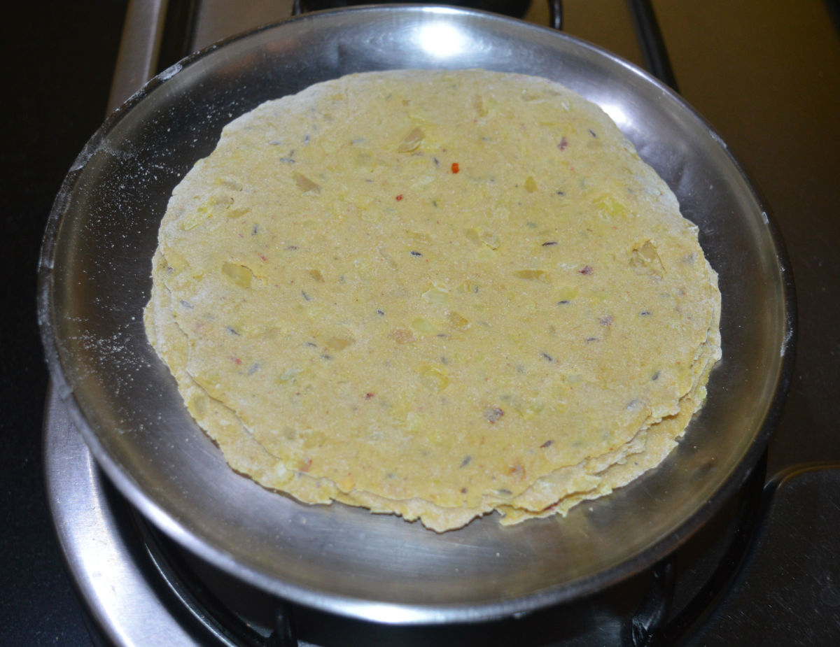 Start working with one patty at a time. Dip it in wheat flour and roll to get an 8-inch diameter disc. Stack them one over the other. These are raw parathas. 
