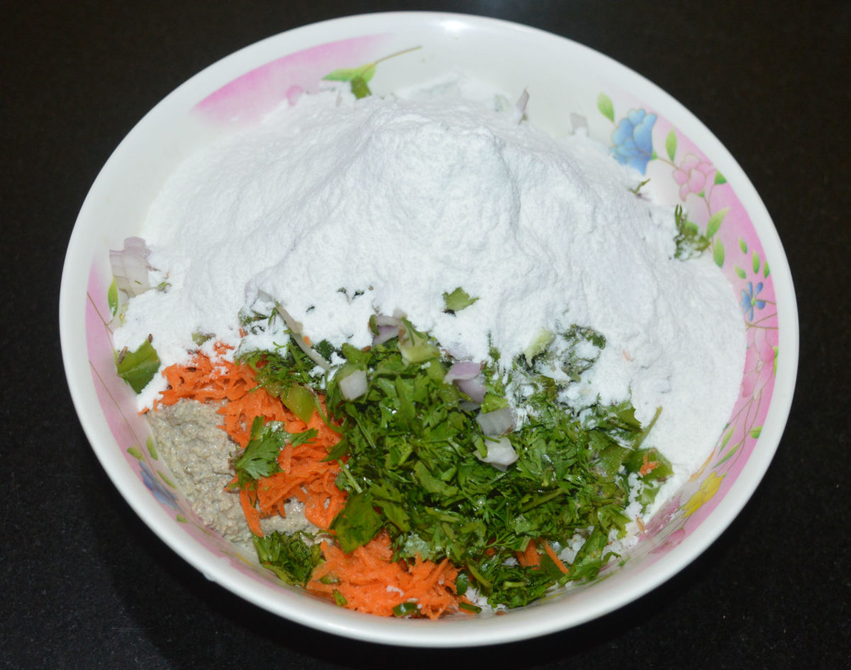 Step three: Add bajra batter to a large mixing bowl. Add rice flour, chopped vegetables, chopped coriander leaves, grated coconut, chopped green chilies, cumin seeds, oil, and salt. Mix well. Make a soft and pliable dough.
