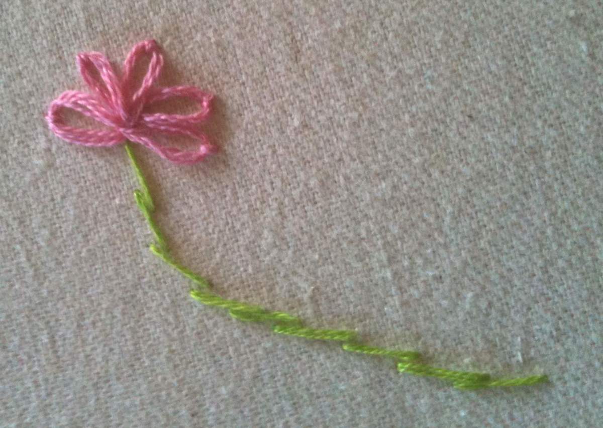 A flower made using lazy daisy stitches (in pink) and stem stitches (in green.)
