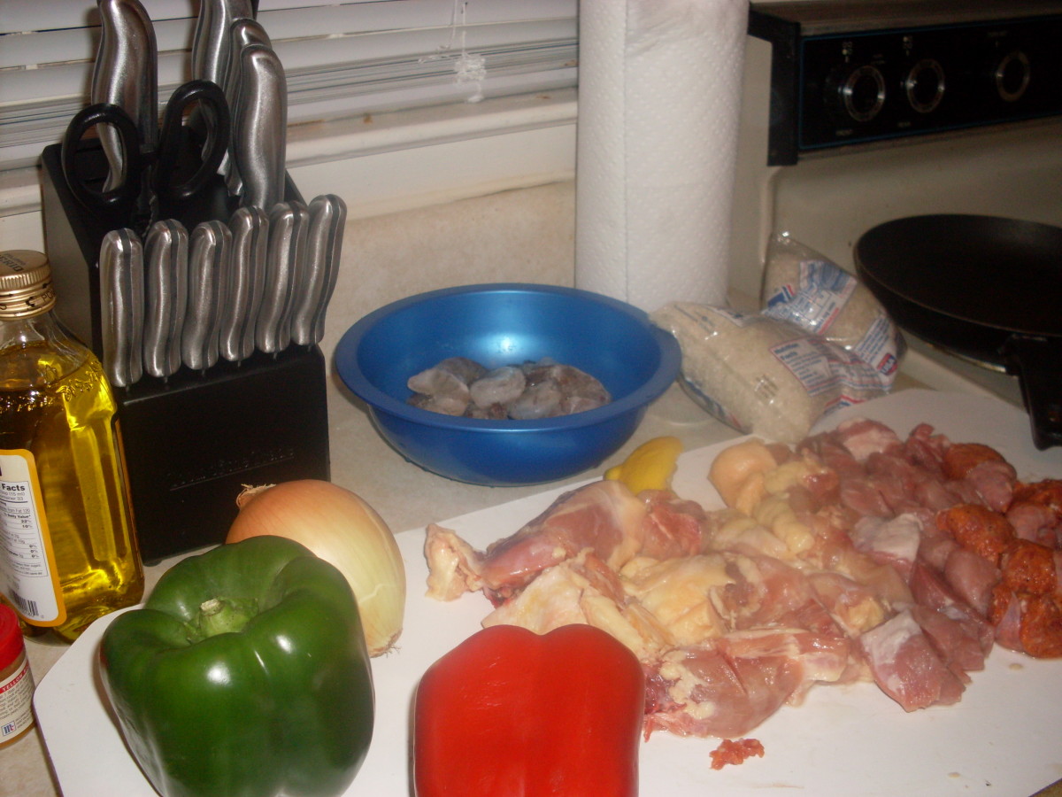 Onion, green bell pepper, red bell pepper, shrimp, rice, chopped raw meat and oil all laid out on the kitchen counter as food prep for getting ready to make this paella.