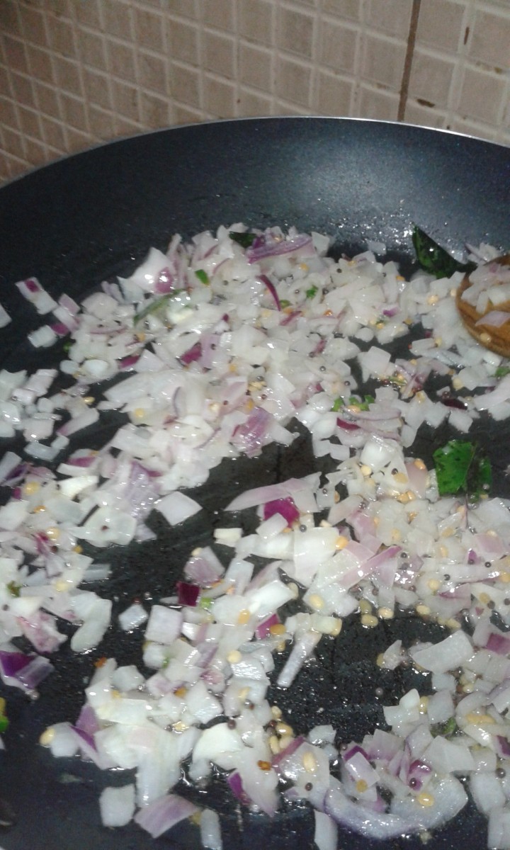 Prepare tempering for upma by heating ghee, add rai, urad daal, hing, curry leaves, green chillies, and onion.