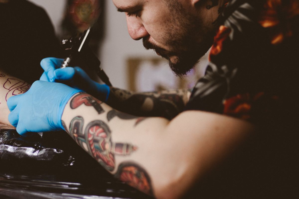 A tattoo artist at work on a patron's arm. Where on your body you choose to place your tattoo can influence how much it costs.