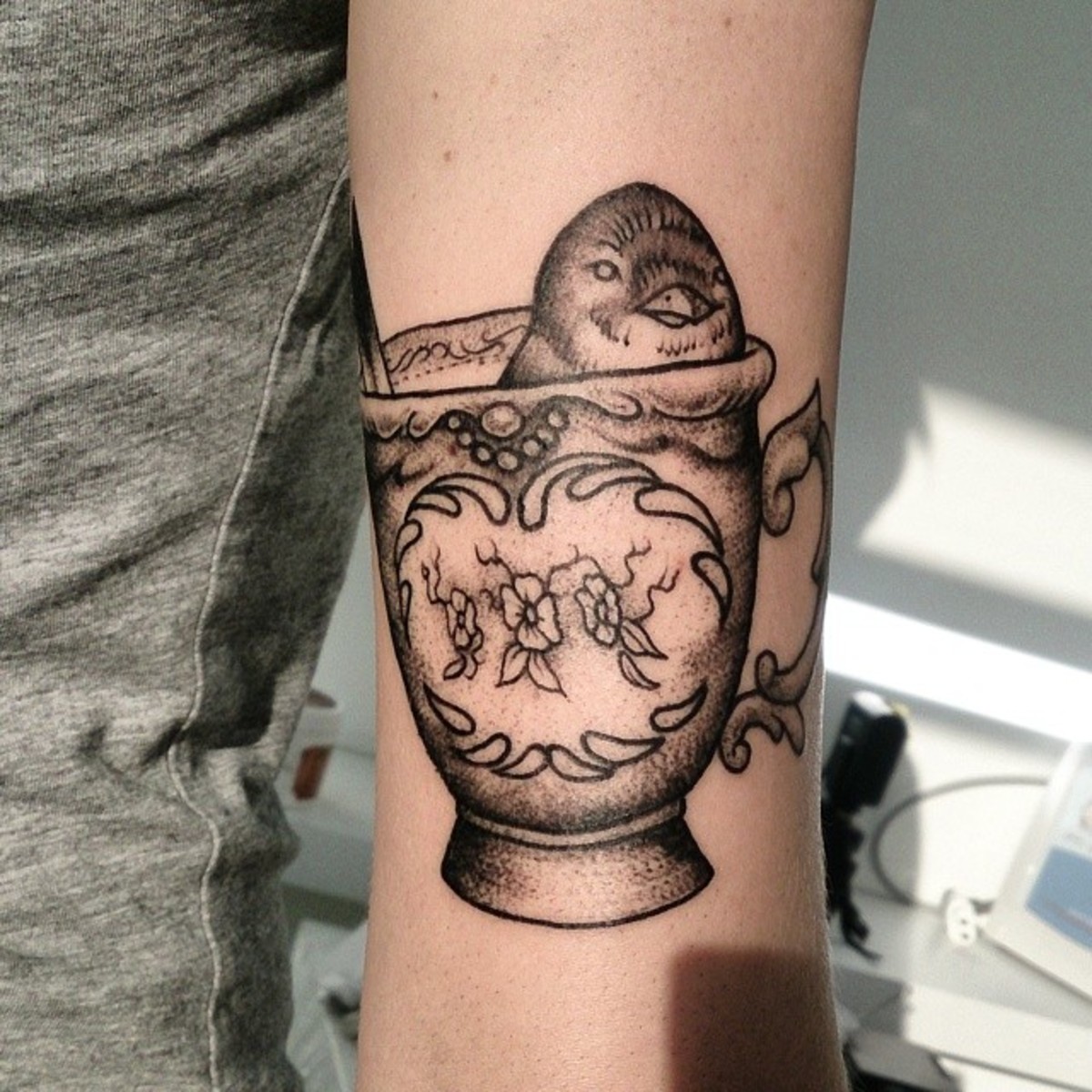 A tattoo of a bird peeping out of a teacup.