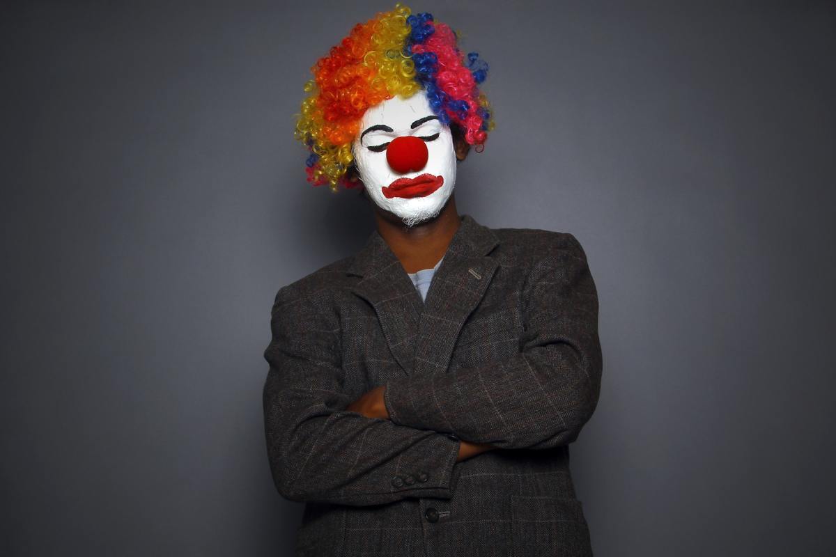 Man dresses with clown makeup but wears corporate attire.
