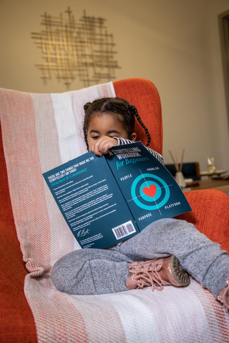 A toddler holding a book in her hands and writing.