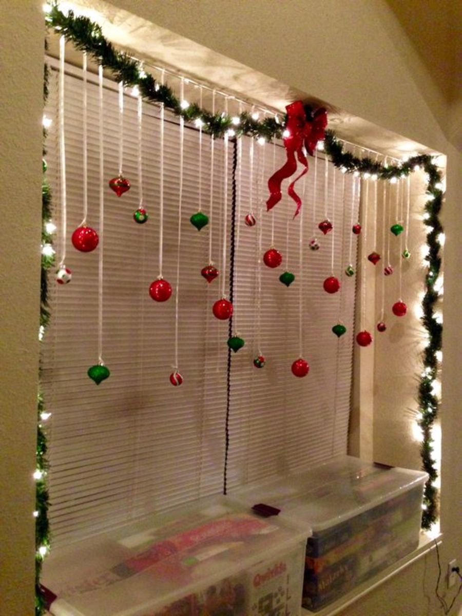 This window features string lights wound around evergreen garlands, ornaments dangling from white ribbons and a big red bow on top.