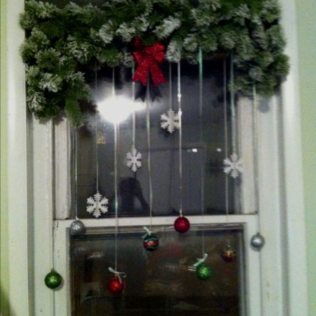 An evergreen swag is the key feature of this cheerful window. Baubles and snowflakes hang from the swag.