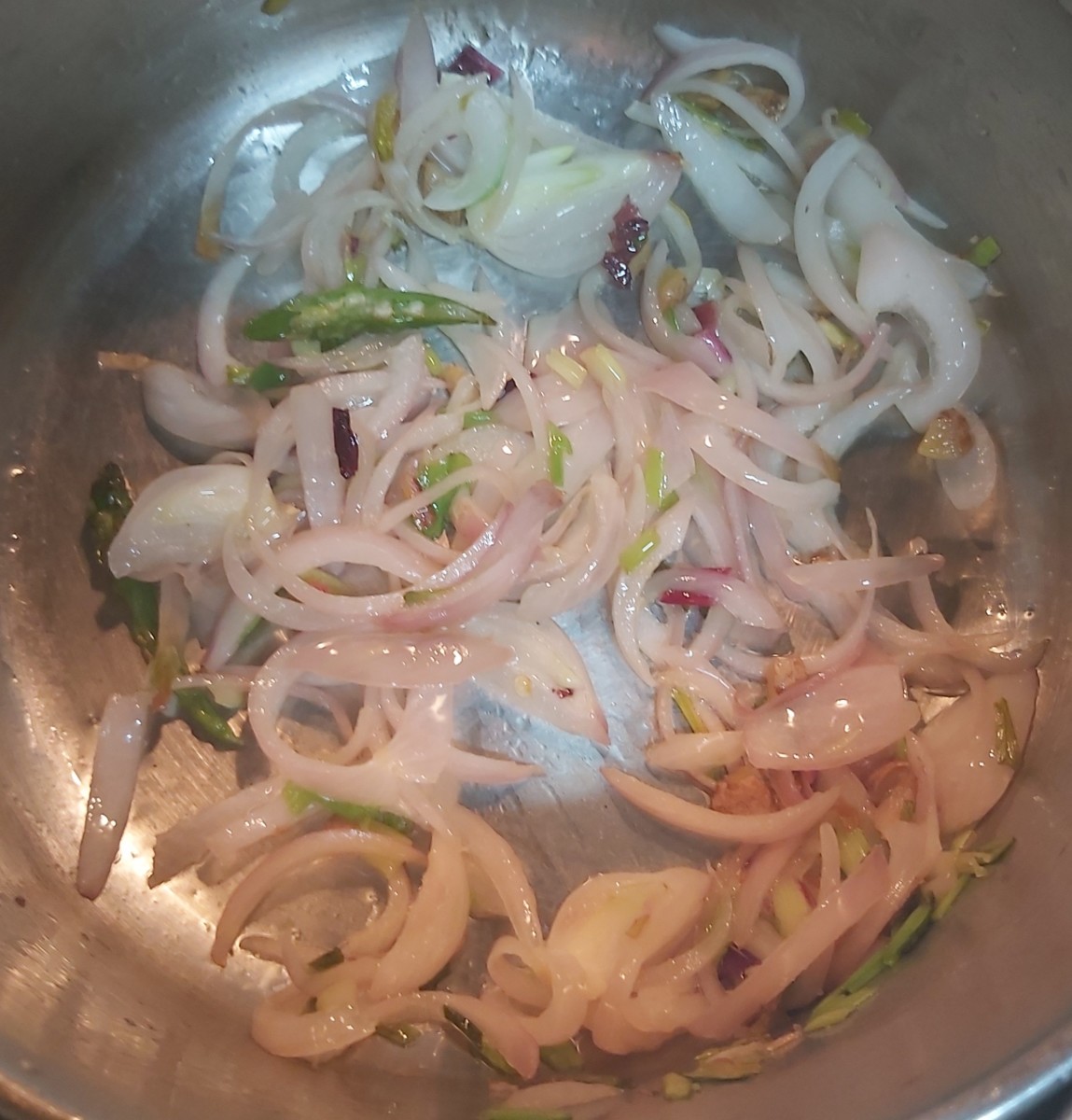 In a pan heat a teaspoon of oil. Add ginger and green chilli. Fry for a few seconds. Add chopped onion and green onion. Fry till the onion turns translucent.