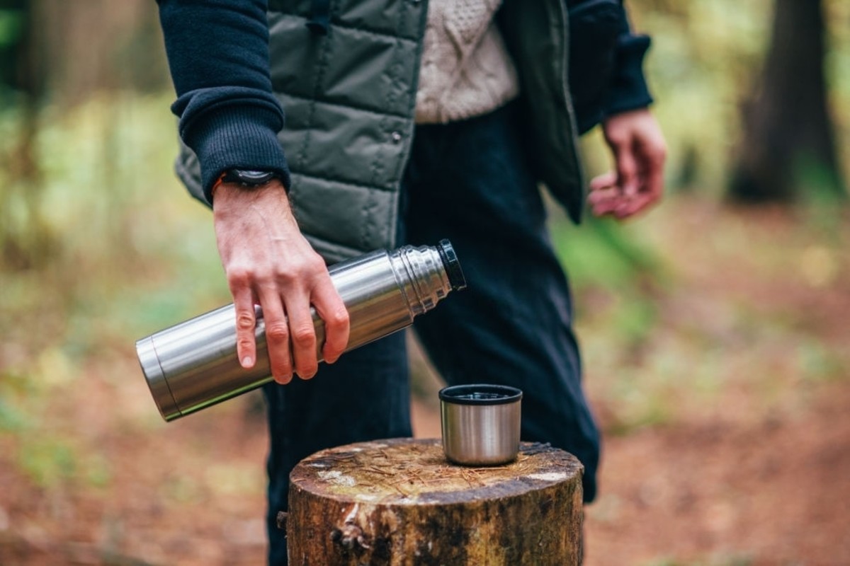 A man pouring tea in the cup from a thermos