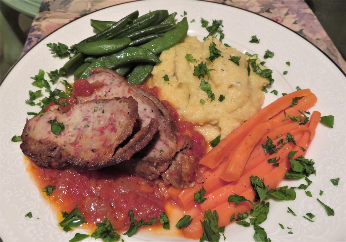  A dinner plate with two slices of braciola atop the delectable sauce, some polenta, carrots, sugar snap peas, and chopped parsley