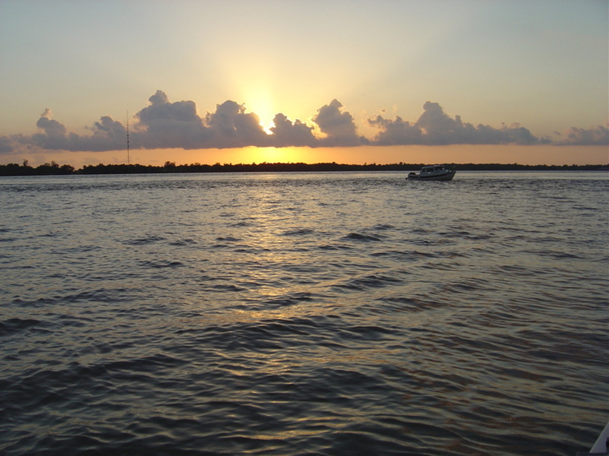 Sunset and clouds create a perfect backdrop for a C-Dory, a small pocket cruiser, anchored for the night at the eastern edge of the lower Mississippi, as the author and her husband prepare to bed down for the night between New Orleans and Venice.