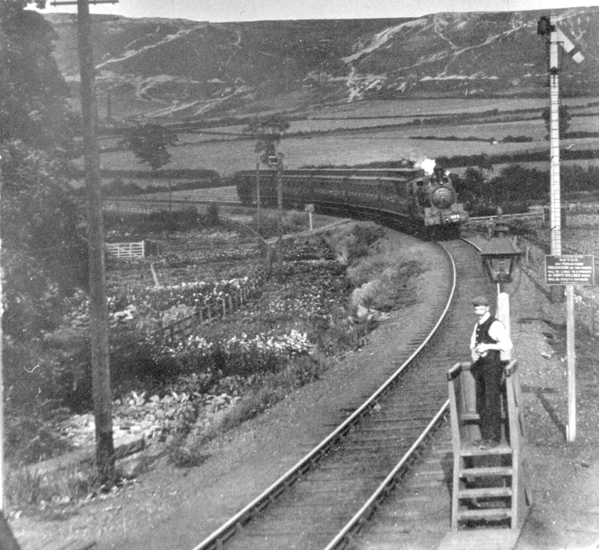 A train arrives at Flatts Lane level crossing from Eston. A 'bobby' (signalman) waits to exchange tokens for the onward section to Whitehouse signal cabin near Middlesbrough