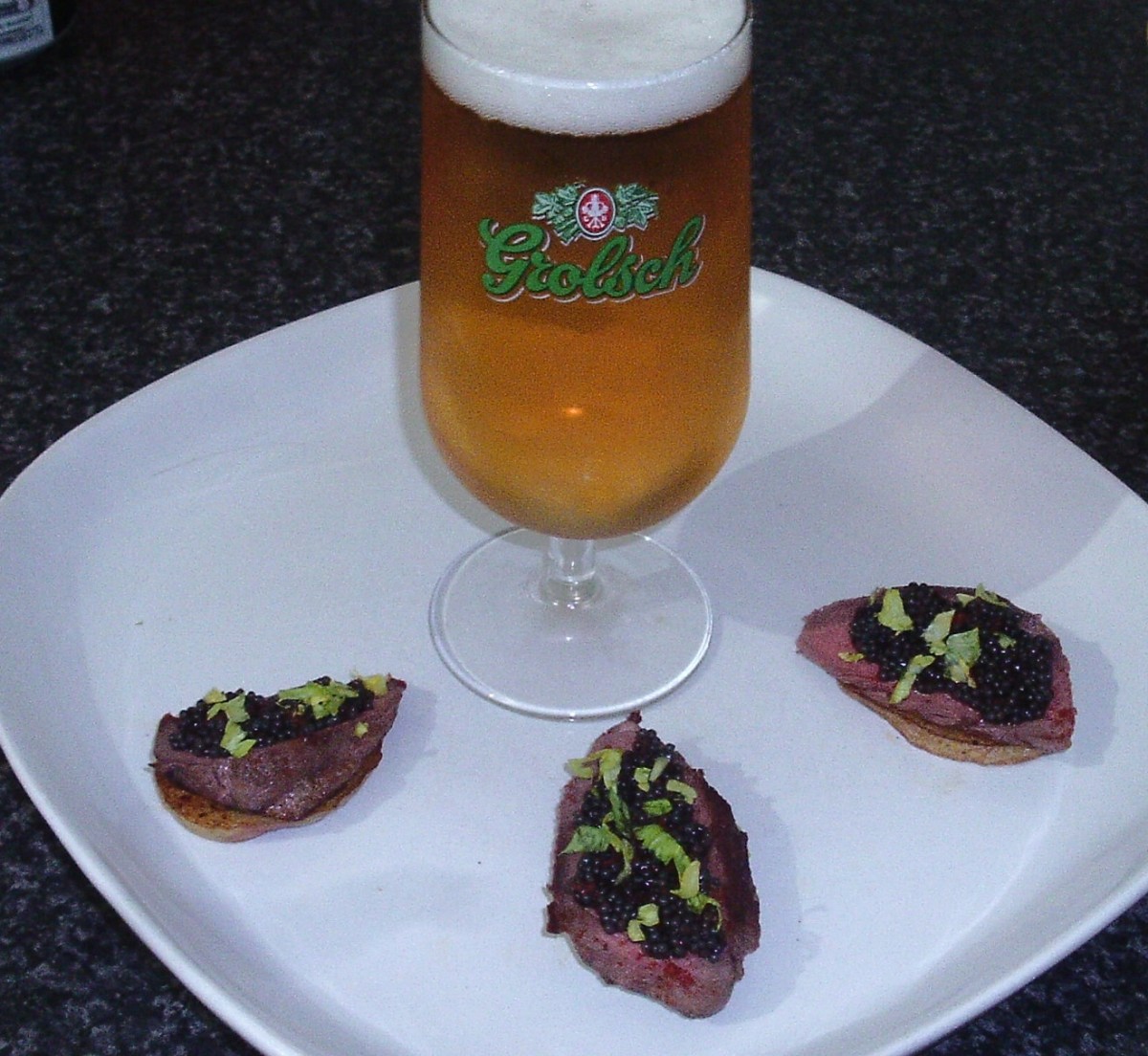 Caviar and sliced pigeon breast on fried potato discs with ice cold beer