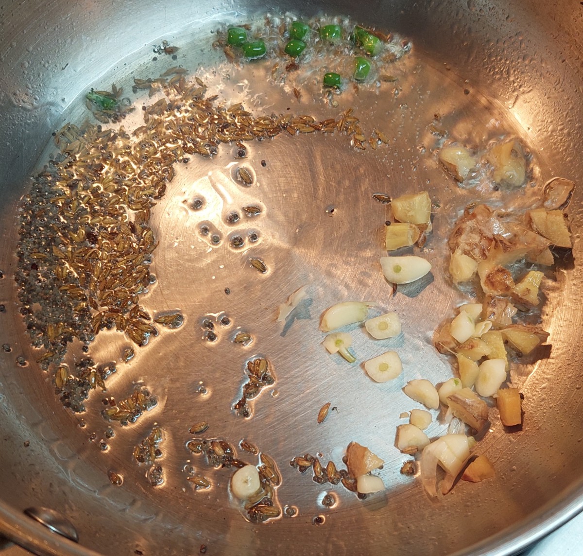 Heat 1 tablespoon of cooking oil in a pan. Add 1/2 teaspoon of mustard seeds and 1 teaspoon of cumin seeds. Let them splutter. Add chopped ginger, garlic and green chilies. Fry for a minute.