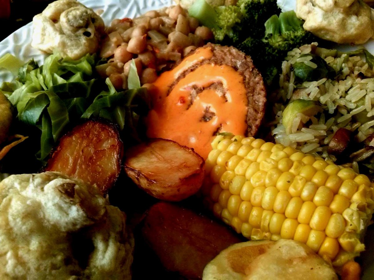 Tempura mushrooms, steamed broccoli, fried brown rice with Brussels sprouts, corn on the cob, roasted baby potatoes, steamed sweetheart cabbage, curried chickpeas with coconut milk, and in the centre a veggie burger with sriracha.