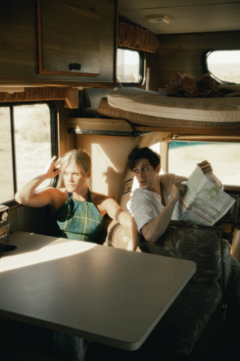 Two friends in a camper van in the middle of nowhere. One is holding a map, telling the other where to go.