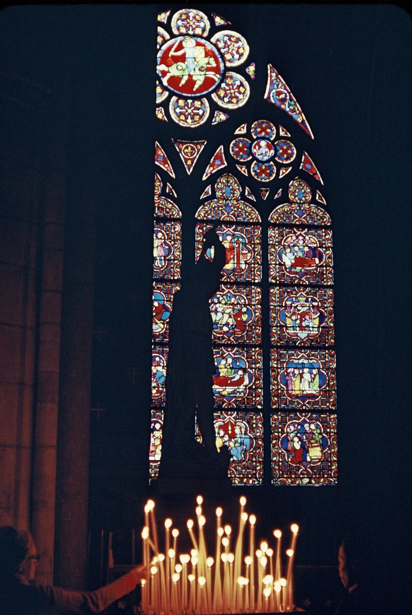 Silhouette of Statue and votive candles in front of one of Notre Dame de Paris Cathedral's stained glass windows