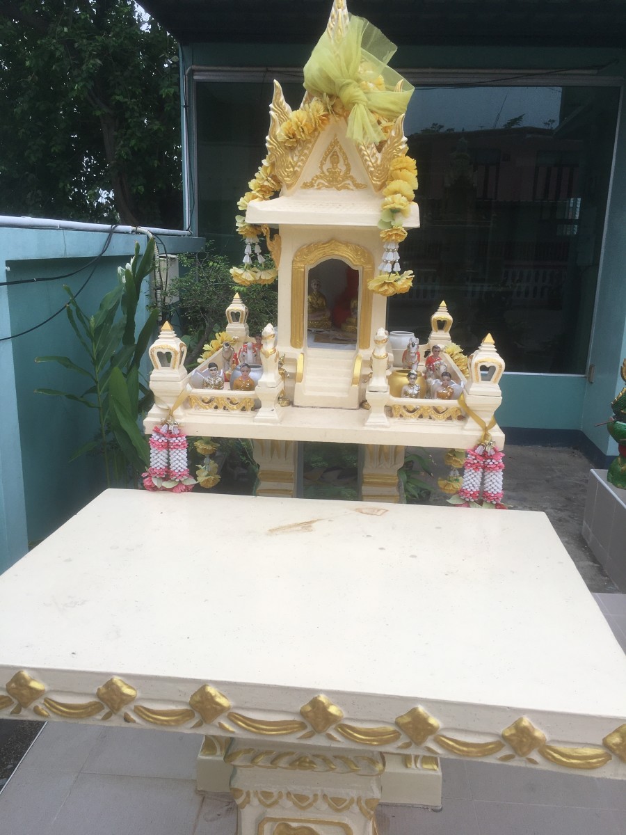 A spirit house on the corner of an apartment building.