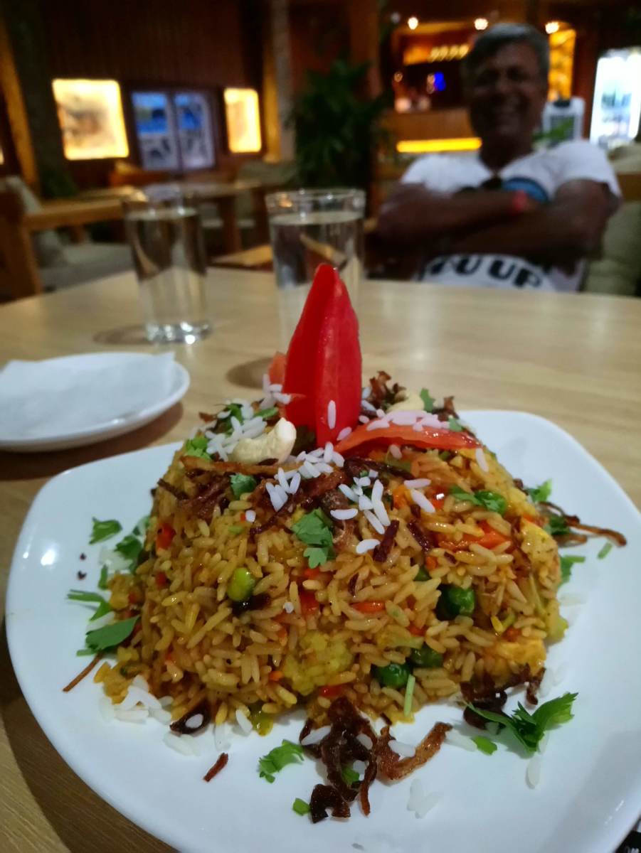 A plate of briyani served at Utopia Garden & Snacks Bar. In the background seats the friendly boss of the restaurant.
