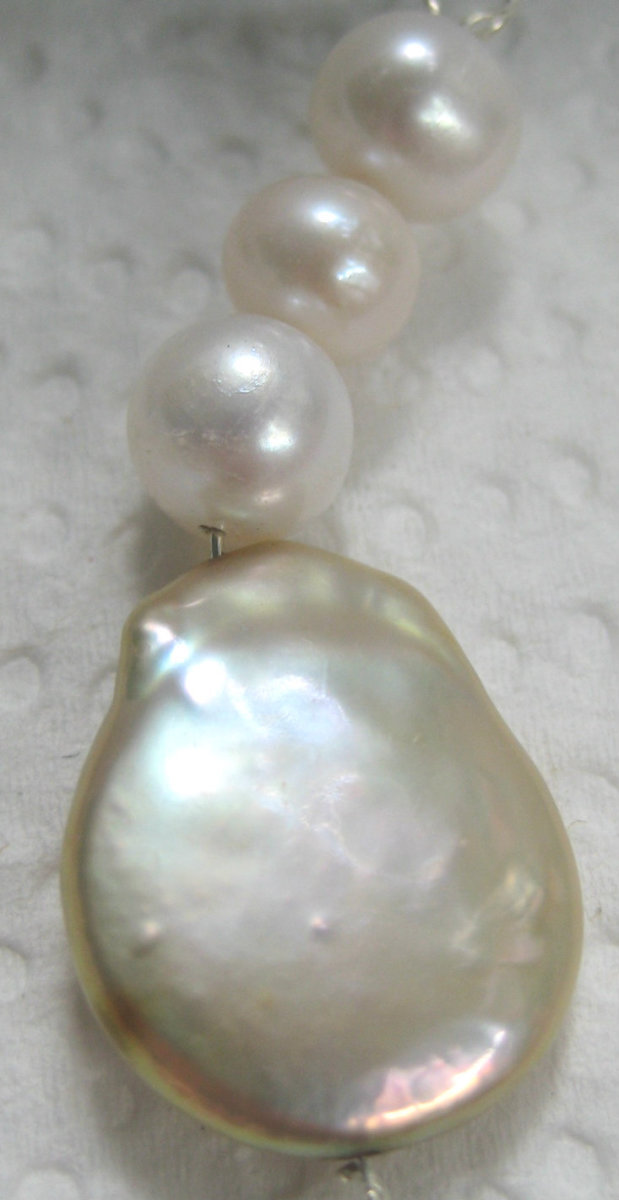 An earring with a gold coin-shaped freshwater pearl, and smaller round white pearls above it. (c) A. Jones 2012