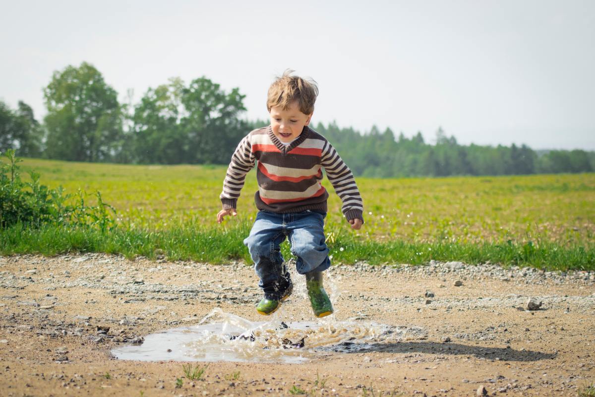 Child jumping on muddy puddle