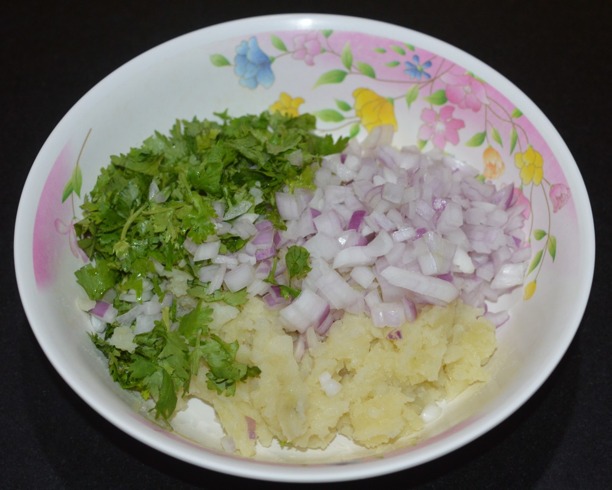 In a mixing bowl, combine the mashed potatoes, chopped onions, chopped spring onion greens (optional), and chopped coriander leaves.