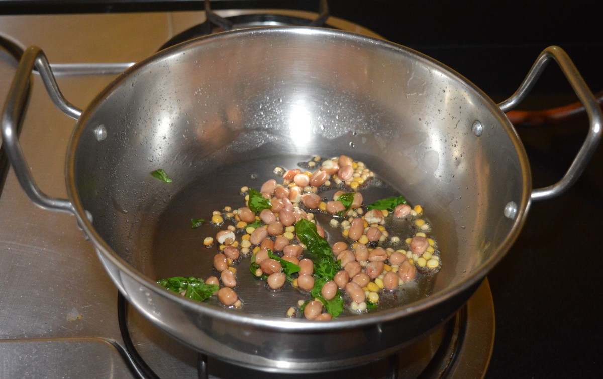 Step two: Heat the oil in a deep-bottomed pan. Throw in mustard seeds and let them crackle. Add peanuts, split chickpea, white lentils, and curry leaves. 