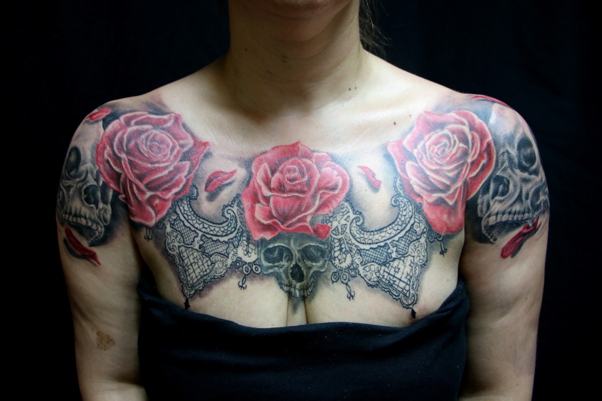 [Woman with a tattoo of large red roses, skulls, and a lace collar covers the clavicle as well as the chest and shoulders.]