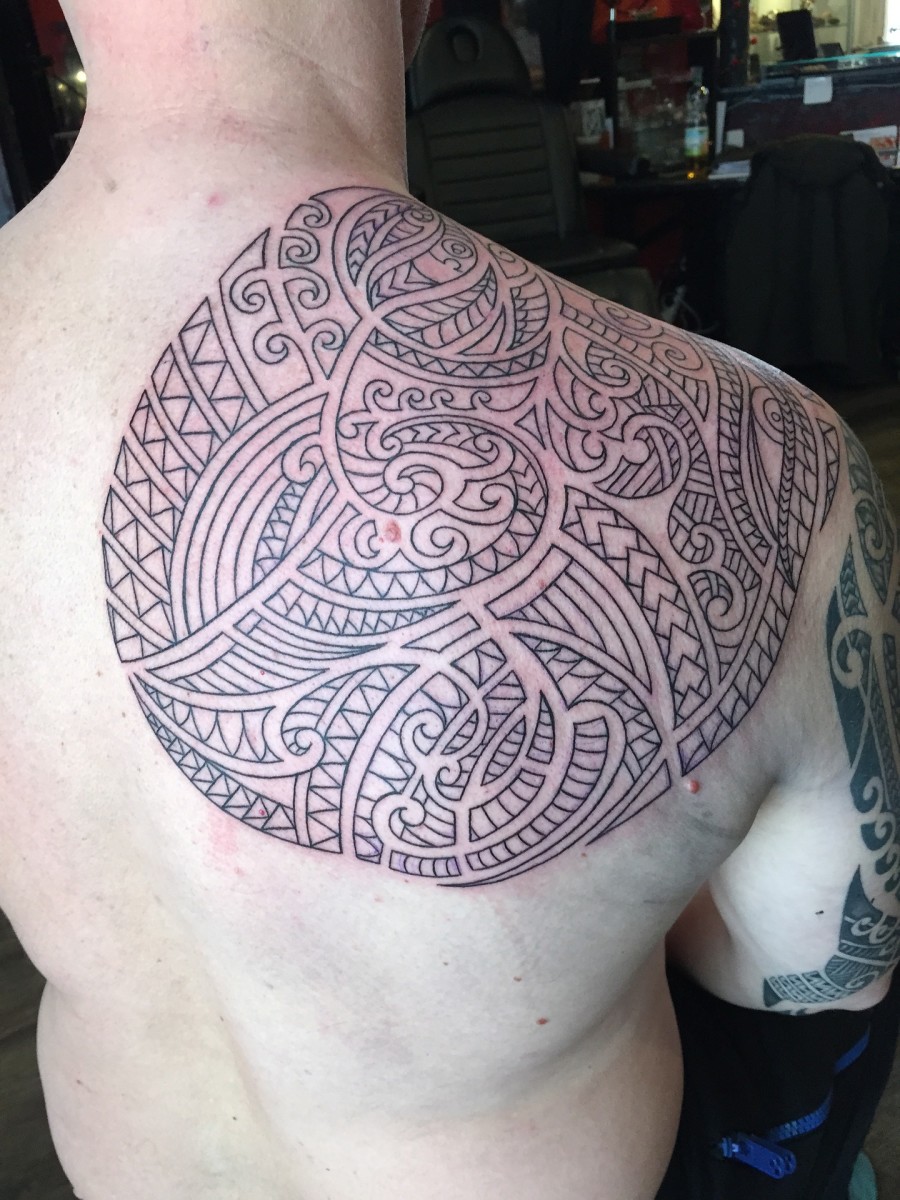 Maori tattoo covering a man's shoulder top, cap, and blade.