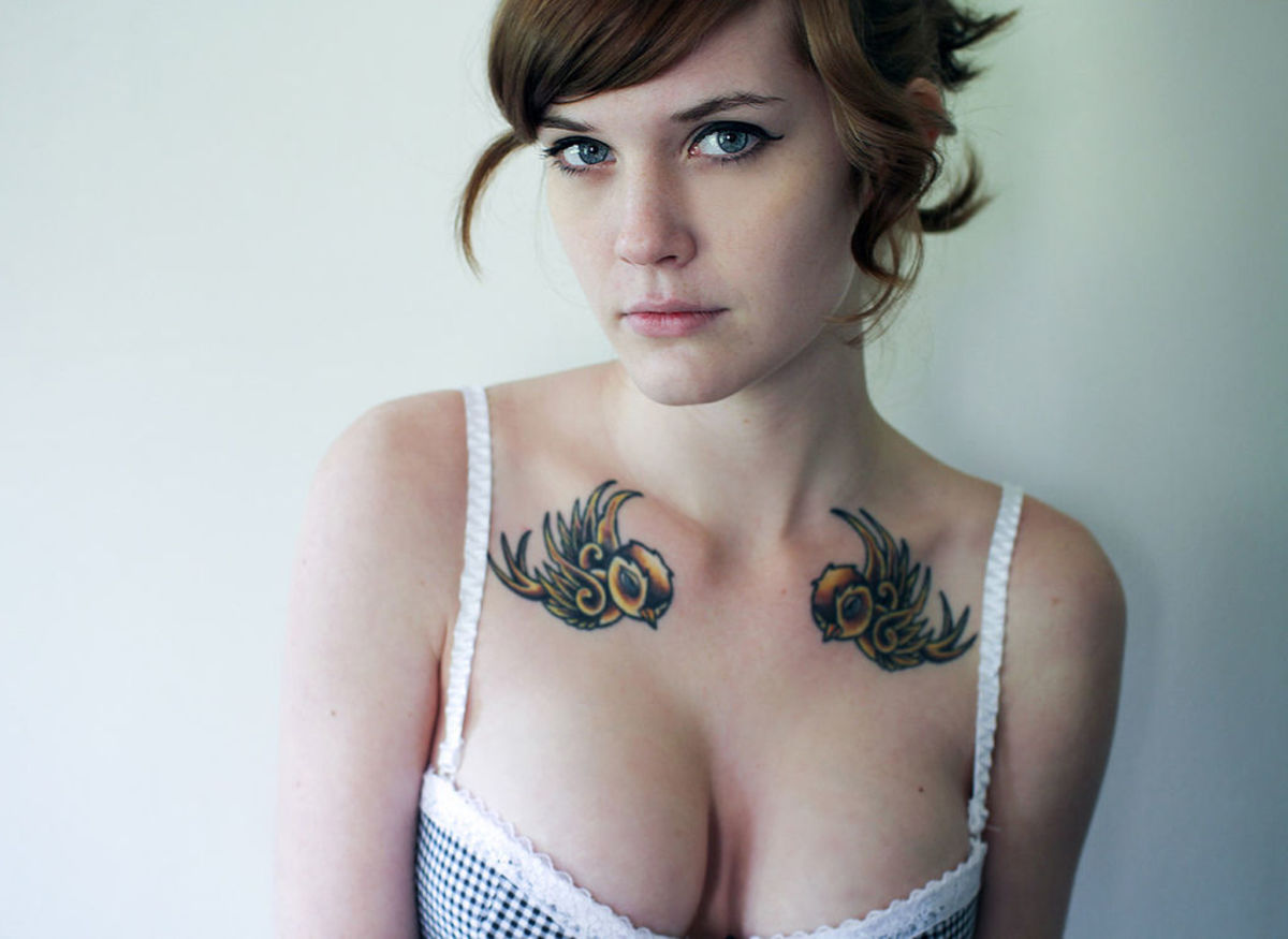Woman with two bird tattoos, one on each side, above her clavicle.