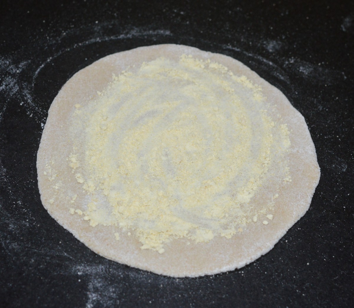 Step three: Divide the dough into many lemon-sized portions. Shape each of the portions to a patty. Roll a patty to make a 4-inch diameter disc. Spread some chickpea flour on it. Also, sprinkle some salt.
