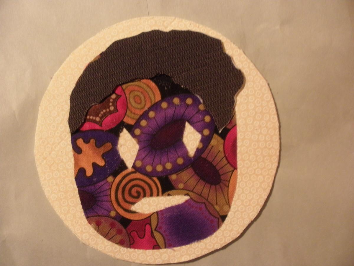 The fabric for this free form mask was first pressed to the Steam-A-Seam 2 before it was cut out of fabric scraps and attached to the coaster background which was made with Fast2Fuse.  The hair is attached using Fast2Fuse for additional dimension.