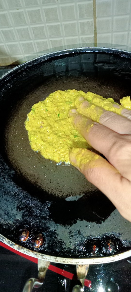 Take a portion of the chilla batter in your hand and slowly spread it on the pan as thinly as possible.