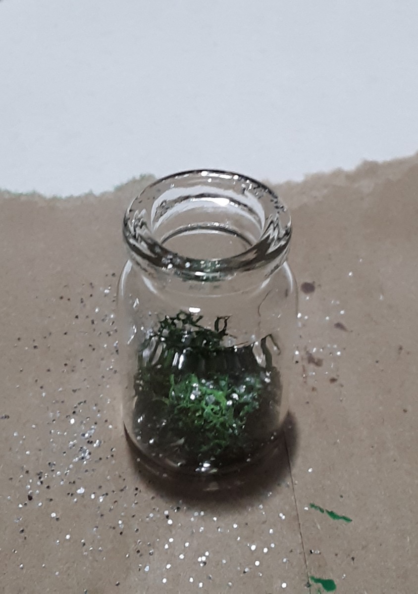 Sprinkle silver glitter inside of the small jar. It will sprinkle nicely on the moss!