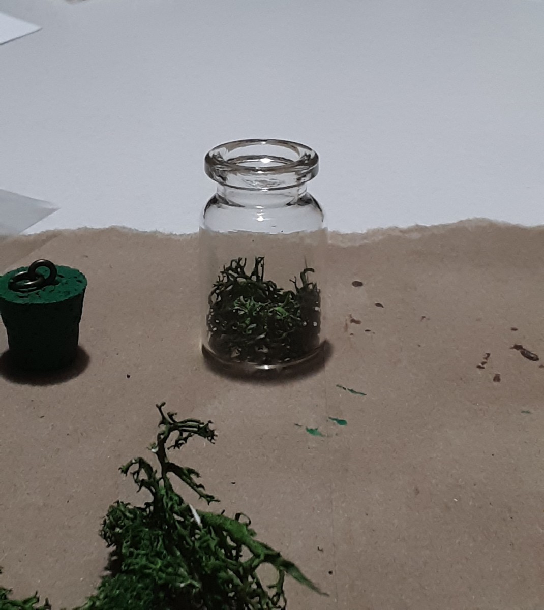 Glue small pieces of the moss inside the bottom of jar. Remember that hot glue dries relatively quickly when putting this craft together.