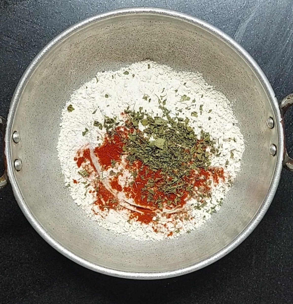 In a wide vessel, add 2 cups of whole wheat flour, salt to taste, 1 teaspoon red chili powder and 1 teaspoon crushed kasuri methi.