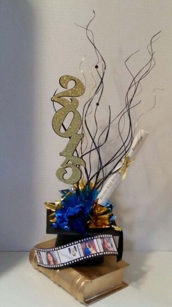 Graduation centerpiece Choose your colors Centerpiece has, Book, picture film, black cap with black tassel, metallic colored fillers, diploma personalized, year in glitter, and wooden swirls. About 2.5 ft tall 